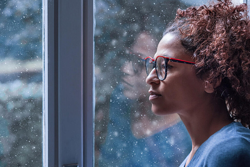 woman with depression looking out the window on a rainy day